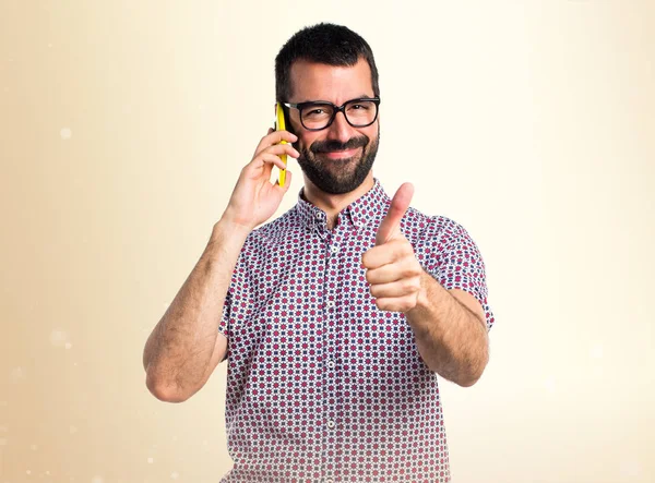 Homme avec des lunettes parlant au mobile sur fond ocre — Photo