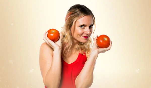 Schöne blonde Frau hält Tomaten auf ockerfarbenem Hintergrund — Stockfoto