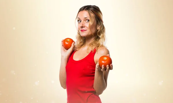 Schöne blonde Frau hält Tomaten auf ockerfarbenem Hintergrund — Stockfoto