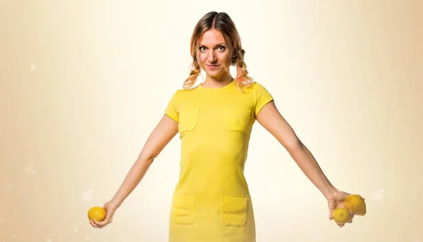 Hermosa mujer rubia sosteniendo limones sobre fondo ocre —  Fotos de Stock