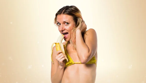 Muz üzerinde koyu sarı backgr tutan bikini güzel sarışın kadın — Stok fotoğraf