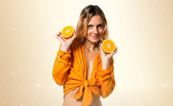 Schöne blonde Frau hält Orangen auf ockerfarbenem Hintergrund — Stockfoto