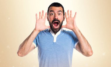 Adam mavi gömlek koyu sarı zemin üzerine sürpriz jest yapıyor