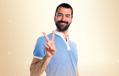 Adam mavi gömlek koyu sarı arka plan üzerinde zafer jest yapıyor