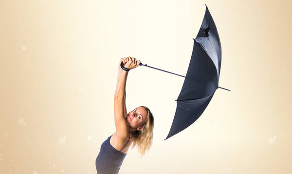 Beautiful blonde girl holding an umbrella on ocher background