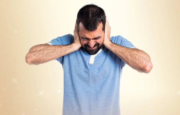 Hombre con camisa azul cubriéndose las orejas sobre fondo ocre —  Fotos de Stock