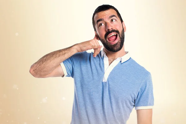 Hombre con camisa azul haciendo gesto de teléfono sobre fondo ocre — Foto de Stock