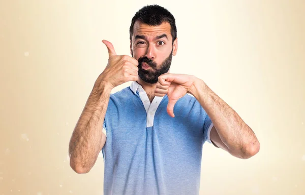 Man met blauwe shirt goed-slecht teken op okergeel achtergrond maken — Stockfoto