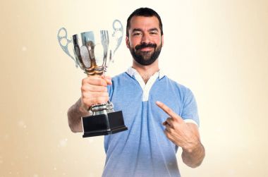 Mavi gömlekli bir kupa koyu sarı arka plan üzerinde tutan adamla