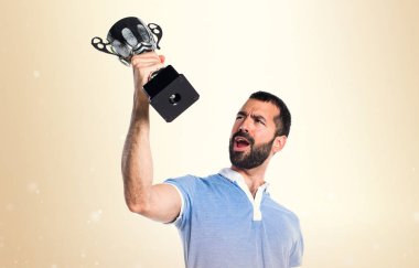 Mavi gömlekli bir kupa koyu sarı arka plan üzerinde tutan adamla