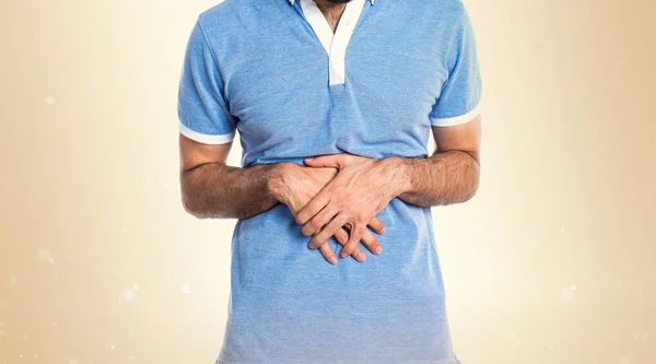 Hombre con camisa azul con dolor de estómago sobre fondo ocre — Foto de Stock