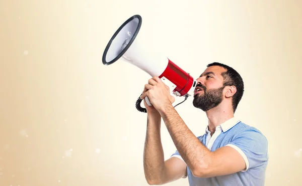 Hombre con camisa azul gritando por megáfono sobre fondo ocre — Foto de Stock