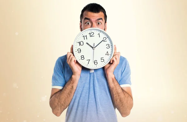 Hombre con camisa azul sosteniendo reloj sobre fondo ocre — Foto de Stock