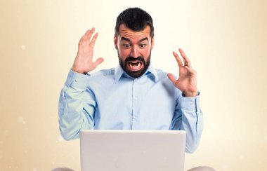 Koyu sarı arka plan üstünde laptop ile sinirli adam