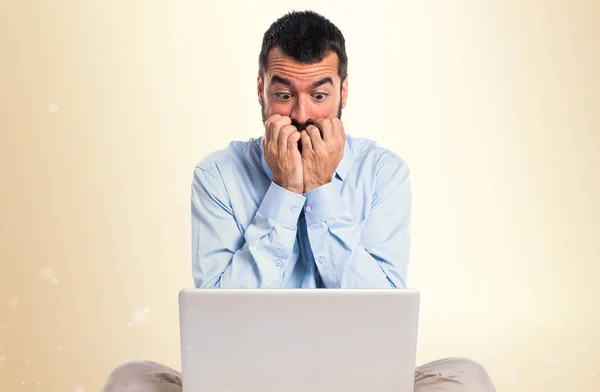 Frightened man with laptop on ocher background