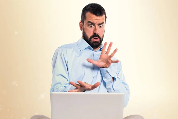 Frightened man with laptop on ocher background