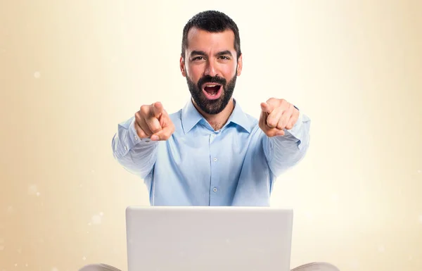 Mann mit Laptop zeigt nach vorne auf ockerfarbenem Hintergrund — Stockfoto