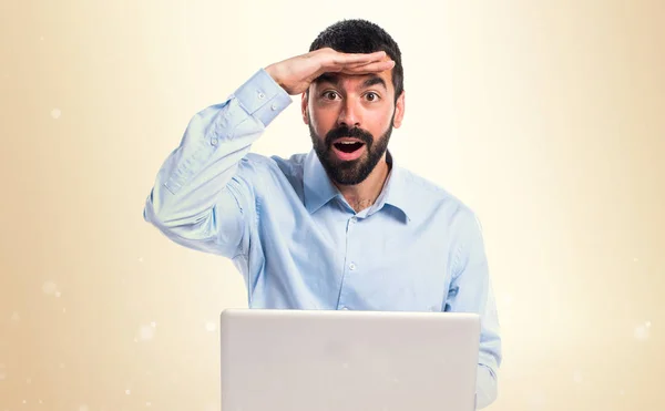Homem com laptop mostrando algo sobre fundo ocre — Fotografia de Stock