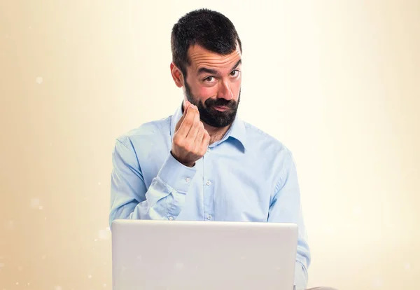 Man met laptop doen geld gebaar op okergeel achtergrond — Stockfoto