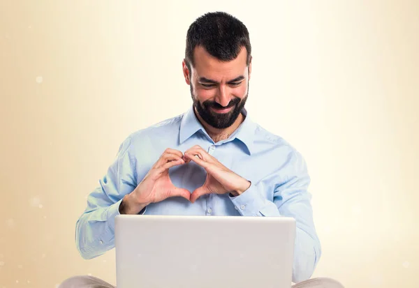 Ο άνθρωπος με το laptop καθιστώντας μια καρδιά με τα χέρια του σε ώχρα backgroun — Φωτογραφία Αρχείου