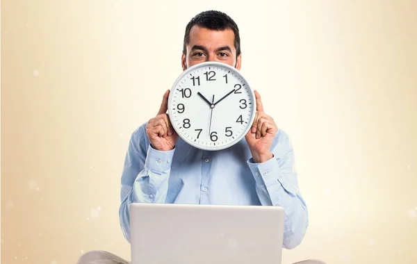 Homem com laptop segurando um relógio no fundo ocre — Fotografia de Stock