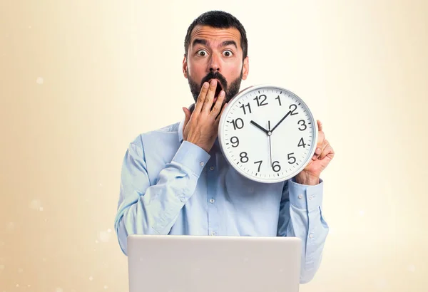 Hombre con portátil sosteniendo un reloj sobre fondo ocre — Foto de Stock