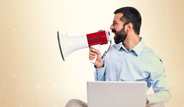 Man met laptop schreeuwen door megafoon op okergeel achtergrond — Stockfoto