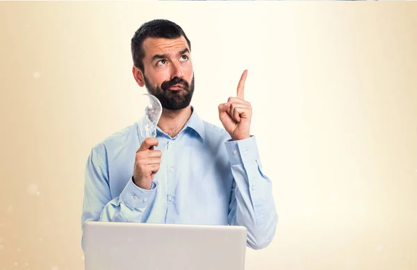 Man met laptop houden een lamp op okergeel achtergrond — Stockfoto