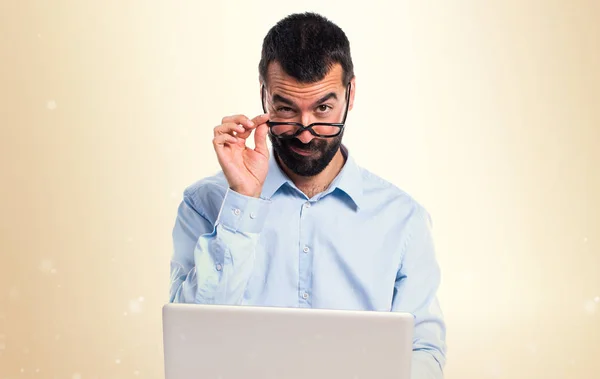 Homem com laptop mostrando algo sobre fundo ocre — Fotografia de Stock