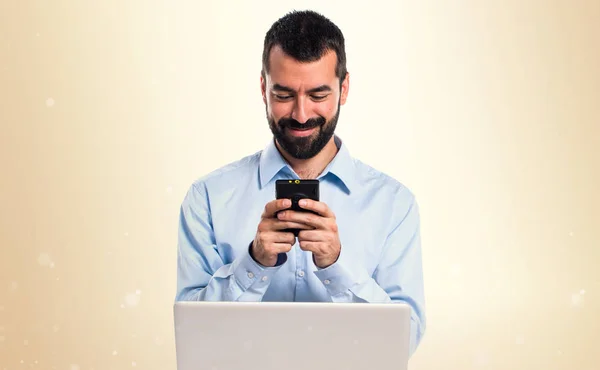 Hombre con el ordenador portátil hablando con el móvil en el fondo ocre —  Fotos de Stock