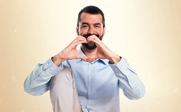 Knappe man die een hart met zijn handen op okergeel achtergrond — Stockfoto