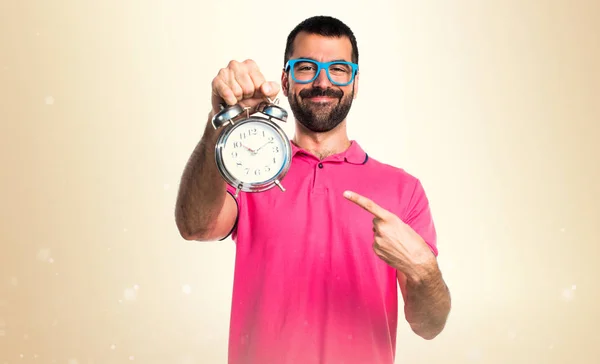 Man with colorful clothes holding vintage clock on ocher backgro — Stock Photo, Image