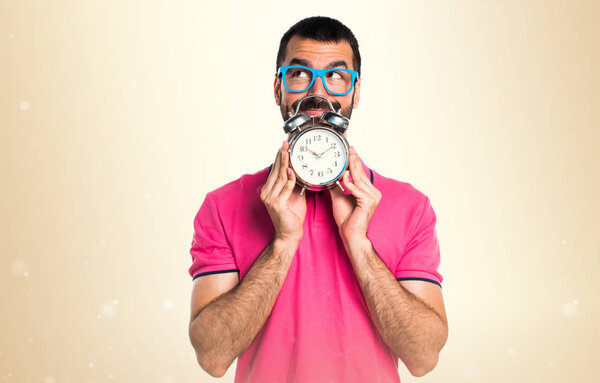 Man with colorful clothes holding vintage clock on ocher backgro