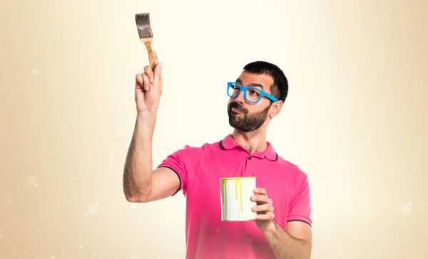 Hombre con ropa colorida sosteniendo una olla de pintura sobre fondo ocre —  Fotos de Stock