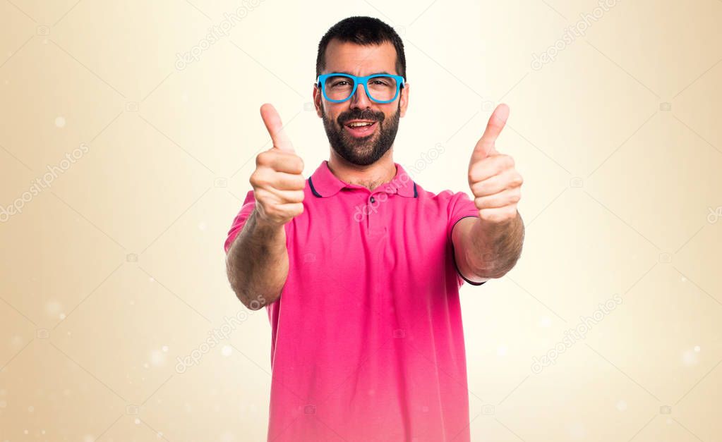 Man in colorful clothes with thumb up on ocher background