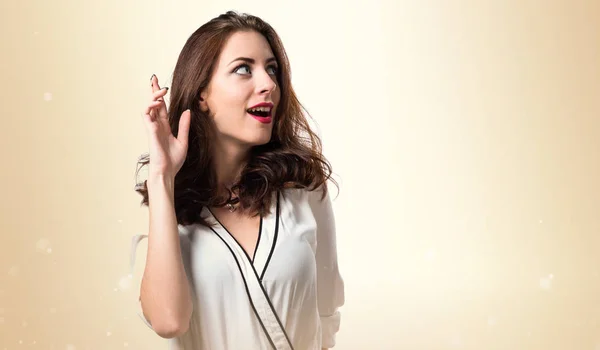 Beautiful brunette girl with his fingers crossing on ocher backg — Stock Photo, Image