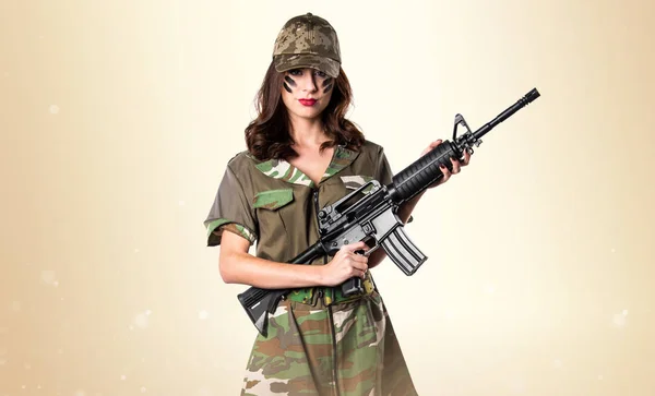 Militära kvinna som håller ett gevär på ockra bakgrund — Stockfoto