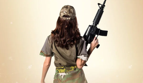 Military woman holding a rifle on ocher background — Stock Photo, Image