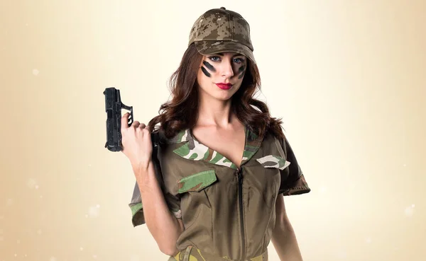 Militära flicka håller en pistol på ockra bakgrund — Stockfoto
