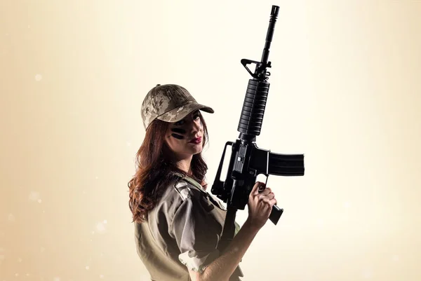 Militära kvinna som håller ett gevär på ockra bakgrund — Stockfoto