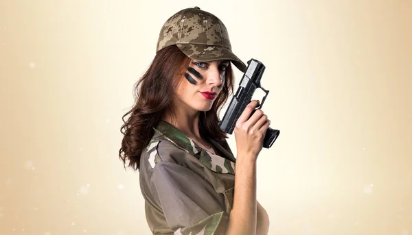 Military girl holding a pistol on ocher background — Stock Photo, Image
