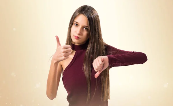 Junges Teenager-Mädchen macht gutes-schlechtes Zeichen auf ockerfarbenem Hintergrund — Stockfoto