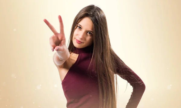 Junges Teenager-Mädchen macht Siegesgeste auf ockerfarbenem Hintergrund — Stockfoto