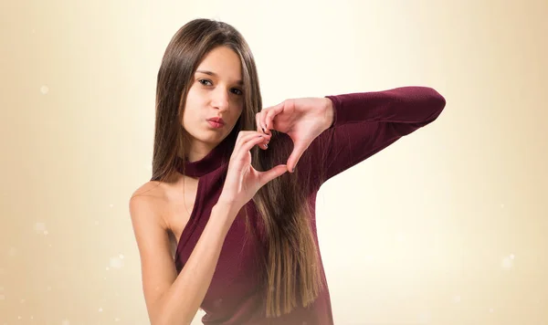 Mädchen macht ein Herz mit ihren Händen auf ockerfarbenem Hintergrund — Stockfoto