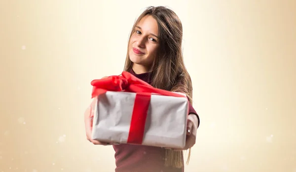 Junges Teenager-Mädchen mit einem Geschenk auf ockerfarbenem Hintergrund — Stockfoto
