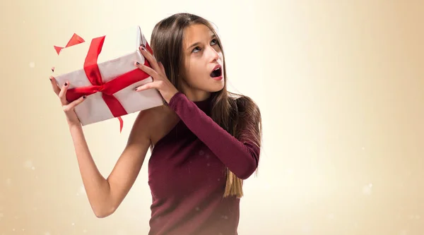 Junges Teenager-Mädchen mit einem Geschenk auf ockerfarbenem Hintergrund — Stockfoto