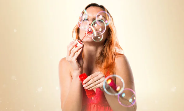 Hermosa mujer con el pelo naranja burbujas que soplan en ocre backgr — Foto de Stock