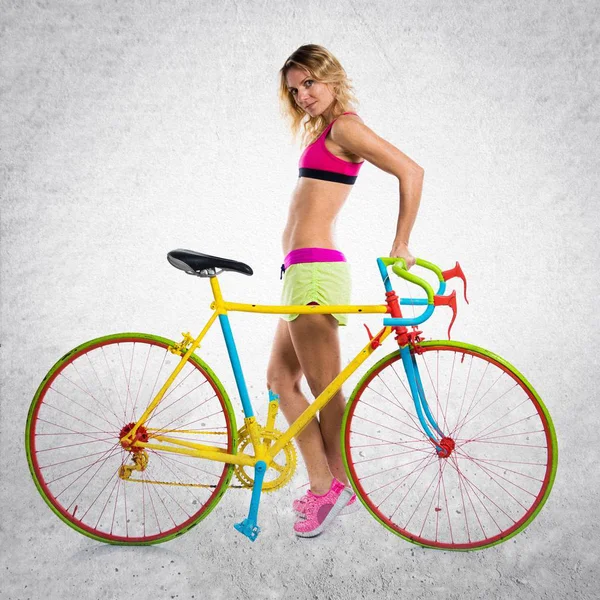 Schöne blonde Frau mit bunten Fahrrad auf strukturiertem Hintergrund — Stockfoto