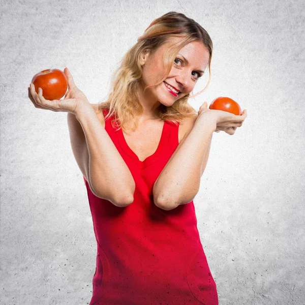Beautiful blonde woman holding tomatoes on textured background
