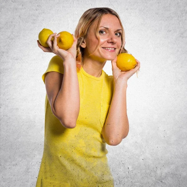 Beautiful blonde woman holding lemons on textured background — Stock Photo, Image